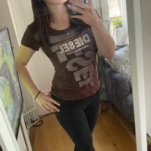 Brun t-shirt från Diesel - Snygg brun t-shirt från Diesel med stort tryck i beige och vitt framtill. Rund hals och korta ärmar. 🌟