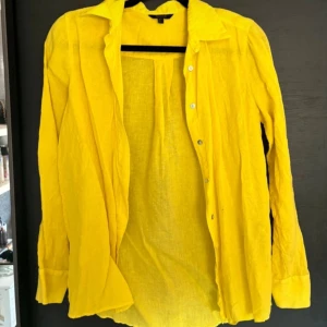 Gul långärmad skjorta Massimo Dutti  - Snygg gul skjorta med långa ärmar och knappar framtill. Perfekt för att lysa upp garderoben med en färgklick. Tillverkad i ett lätt och bekvämt material.