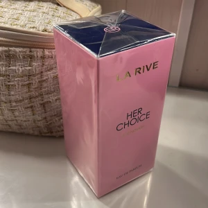La Rive Her Choice Eau de Parfum - Elegant och feminin parfym från La Rive, Her Choice, i en stilren rosa förpackning. Flaskan innehåller 100 ml av en doft skapad i Frankrike, perfekt för den som söker en sofistikerad och modern doftupplevelse.  