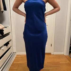 Blå axelbandslös klänning - Elegant blå axelbandslös klänning i satin med en vacker öppen rygg och knytning. Perfekt för speciella tillfällen. Endast använd en gång. Pris kan diskuteras.