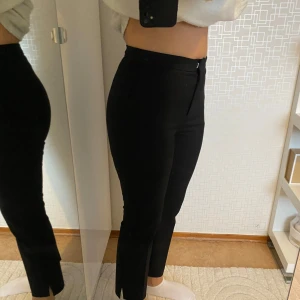 Svarta byxor med slits - Snygga svarta byxor med hög midja och tight passform. Byxorna har en diskret slits vid anklarna och stängs med dragkedja. Perfekta för en stilren look.