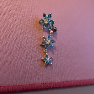Silver blå blomformade Navelpersing  - Snygga Navelpersing med tre blå blommor i rad, varje blomma har en glittrande sten i mitten. Perfekt för att ge en färgklick till din outfit. De hänger elegant och fångar ljuset vackert.
