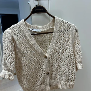 Beige stickad kofta från Zara i 84% bomull  - Säljer en söt beige stickad kofta från Zara med korta ärmar och knappar framtill, bomull. 