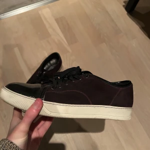 Lanvin - skor - Tjena! Tänkte sälja vidare min skor som stått på hyllan ett tag. Med andra ord är de knappt använda, max två gånger. Det är en snygg vinröd/svart sneaker med snörning och vit sula. Skorna har en stilren design med en blank tådel och är perfekta för en avslappnad look. Eller ifall man vill gå mot det lite finare hållet. Hojta till ifall det är någon fråga eller så👍