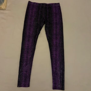 Lila leggings med ormmönster - Snygga lila leggings med ett coolt ormmönster. Perfekta för att ge din outfit en unik touch. De är stretchiga och bekväma, vilket gör dem idealiska för både vardag och speciella tillfällen.
