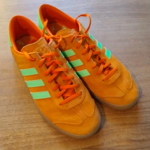 Orange Adidas sneakers - Snygga orange sneakers från Adidas med gulgröna detaljer och klassiska ränder. Skorna har en gummisula och snörning för en bekväm passform. Perfekta för en färgglad stil. Precis köpta. Sparsamt använda. 