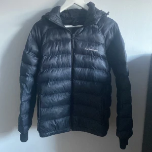 Svart dunjacka från Peak Performance - Säljer min svarta dunjacka från Peak Performance med huva och dragkedja då den blivit för liten för mig. Perfekt för kyliga dagar med sin quiltade design som håller värmen. Storlek 170