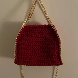 Vinröd virkad väska - Handgjord supersöt stellamccartney liknande väska. Vinröd med guldig kedja. Ingår även en lång kedja och en magnetknapp inuti. Väskan är ungefär 20x18 och rymmer väldigt mycket!! ❤️❤️