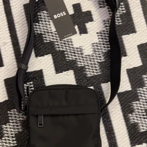 Svart axelväska från BOSS - Helt ny BOSS Väska till ett billigt pris. Köpte den ny för 1100kr. Den har inte kommit till nån användning för min del så nu va det dags att göra sig av med den. Hör av er om ni är intresserade eller har några frågor!