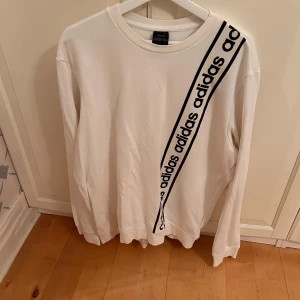 Vit sweatshirt från Adidas - Säljers en snygg vit sweatshirt från Adidas i storlek XL. Tröjan har en cool svart logga längs ena sidan och är perfekt för både vardag och träning. Den är i mycket bra skick och superbekväm att ha på sig. Passar perfekt till höst och vår!