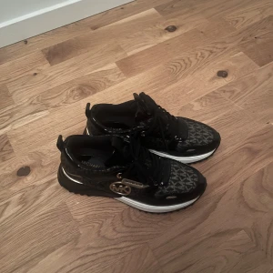 Svarta sneakers från Michael Kors - Snygga svarta sneakers från Michael Kors med gulddetaljer och logotyp. Skorna har ett mönster med märkets initialer och är i mycket bra skick. Perfekta för både vardag och festliga tillfällen. De har en bekväm passform och snörning framtill. Storlek 38 ord pris 2300 kr. Pris kan diskuteras!