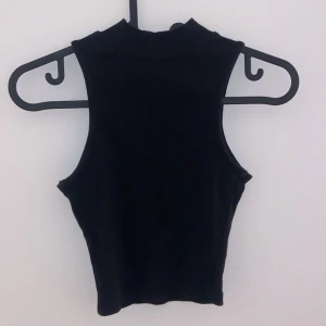 Svart ärmlös topp - Snygg svart ärmlös topp i ribbat material. Perfekt för sommardagar eller som ett lager under en jacka. Den har en tight passform som framhäver figuren. Enkel och stilren design som passar till allt!