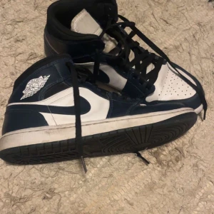 Nike Air Jordans i svart och vit - Säljer ett par Nike Air Jordans i svart och vit. Skorna har en klassisk hög modell med snörning och den ikoniska Air Jordan-loggan på sidan. De är i bra skick med lite slitage på sulorna. Perfekta för både vardag och sportiga tillfällen!