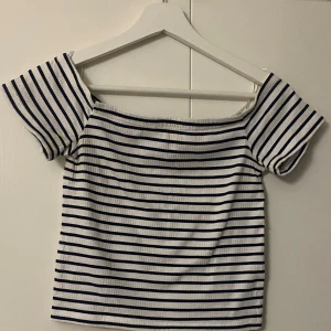 Randig offshoulder topp - Säljer en superfin vit och svart randig offshoulder topp. Perfekt för sommardagar och ger en härlig marin känsla. Toppen är i ett mjukt och stretchigt material som sitter skönt på kroppen. Passar perfekt till både jeans och kjol! 