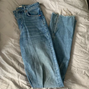 Blå jeans med fransig kant - Säljer ett par snygga blå jeans med slits nertill. De har en klassisk femficksdesign och en ljus tvätt som ger en avslappnad look. Perfekta för vardagsbruk och kan stylas med nästan vad som helst. Passar bra till både sneakers och boots.
