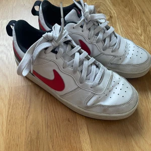 Vita och röda Nike airforces - Säljer ett par vita Nike sneakers med röda detaljer och snörning. De har en klassisk design med en röd Nike-logga på sidan. Perfekta för vardagsbruk och ger en sportig look. Skorna är i bra skick med lite slitage på sulan.