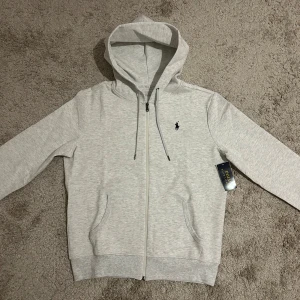 Ralph Lauren Zip Hoodie Ljus Grå - Säljer min Ralph Lauren zip då den inte passar mig. 10/10 skick, oanvänt. Skriv gärna för mer information! 