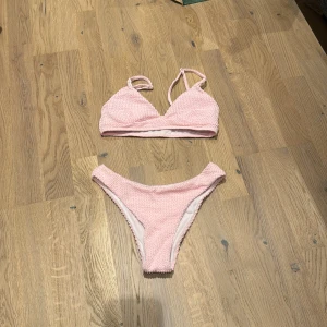 Rosa bikini i ribbat material - Säljer en superfin rosa bikini i ribbat material. Toppen har justerbara axelband och en bekväm passform. Perfekt för sommarens stranddagar eller poolhäng. Bikinibyxorna har en klassisk skärning som sitter snyggt. Aldrig använt då storleken inte passa mig, så den är i mycket bra skick. 🌸