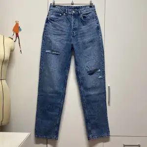 Säljer ett par snygga blå jeans med coola slitningar på låren. De har en klassisk femficksdesign och en straight passform som ger en avslappnad look. 