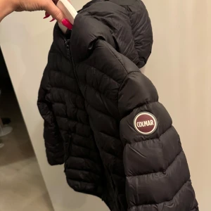Svart dunjacka från Colmar strl 142 - Säljer en snygg svart dunjacka från Colmar i mycket bra skick. Jackan har en quiltad design med dragkedja framtill och en liten logga på ärmen. Perfekt för kyliga dagar och ger en stilren look. Passar både till vardags och lite finare tillfällen. Strl 142