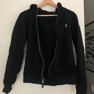 Svart hoodie från Ralph Lauren - Säljer en svart hoodie från Ralph Lauren i bra skick. Den har en dragkedja framtill och en liten logga på bröstet. Perfekt för höst och vår, med långa ärmar