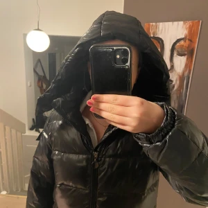 Svart pufferjacka med huva - Jag säljer en pufferjacka från nuvelle. Den är helt oanvänd och säljer den pga. fel storlek. Märket på armen går att ta bort för den sitter fast med kardborre. Köparen betalar frakten. 
