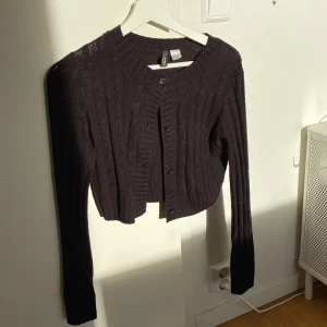 Mörkbrun stickad kofta från H&M - Säljer en superfin svart stickad kofta från H&M i storlek XS. Den är croppad och har långa ärmar med knappar framtill. Perfekt för höst och vinter, och den är i mycket bra skick. Passar både till vardags och fest!