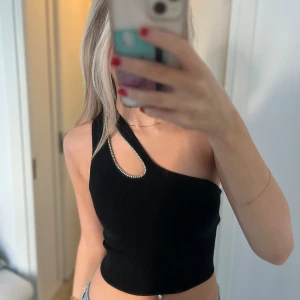 Svart oneshoulder topp från H&M - Snygg svart oneshoulder topp från H&M i ribbat material. Den har en unik design med en glittrig detalj runt axelbandet. Perfekt för en utekväll eller fest! Toppen är i mycket bra skick och passar perfekt till jeans eller kjol.