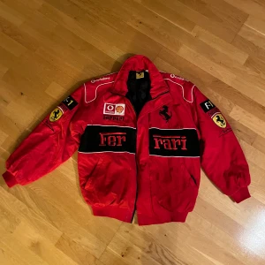 Vintage 90s Nasqar Ferrarijacka röd - Säljer en vintage 90s röd nasqar Ferrari jacka med coola loggor och broderade detaljer. Jackan har dragkedja och långa ärmar, perfekt för racingfans. Detta är den riktiga vintagejackan som de nyproducerade är kopierade av. 