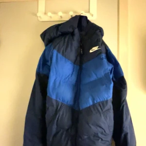 Blå och svart vinter från Nike - Säljer en snygg blå och svart dunjacka från Nike i storlek S. Jackan har en dragkedja och en huva, perfekt för kalla dagar. Den är i mycket bra skick och passar både höst och vinter. Perfekt för dig som vill hålla stilen när det är kallt ute!  ( Den kostar 1400kr helt ny) priset kan diskuteras ner 