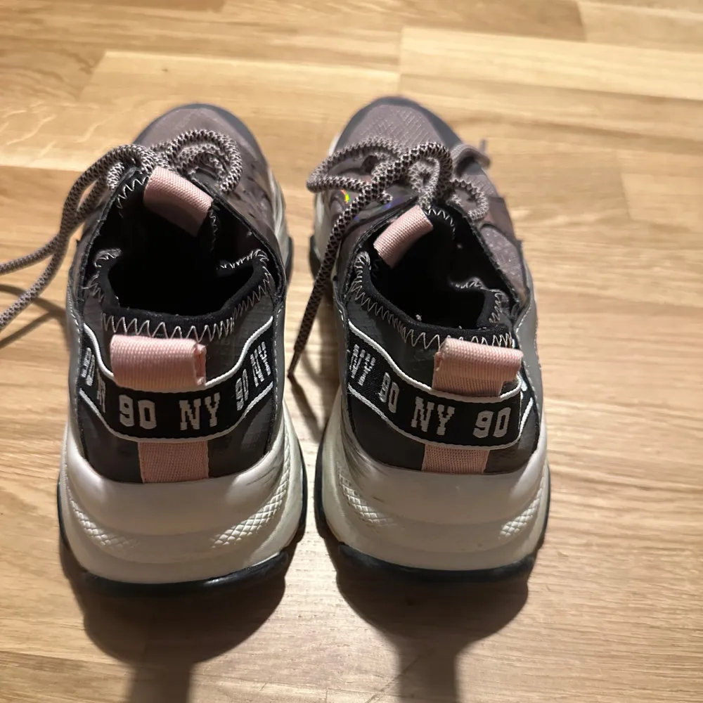 Säljer ett par Steve Madden sneakers i grått med coola rosa detaljer och snörning. De har en chunky sula och texten '90 NY' på sidan. Perfekta för en trendig look!. Kengät.