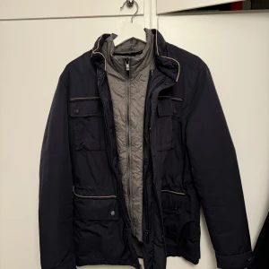 Mörkblå jacka från Massimo Dutti - Säljer en snygg mörkblå jacka från Massimo Dutti. Den har en stilren design med dragkedja och knappar framtill. Jackan har flera praktiska fickor och en bekväm passform. Den har lite defekter på knapparna annars är skicket mycket bra! 