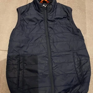 Mörkblå väst från X-Trail i storlek 160 - Säljer en svart väst från X-Trail i mycket bra skick. Västen är perfekt för höst och vår, eller ha under en jacka.. Dragkedja framtill och två fickor. Tillverkad i 100% polyester, vilket gör den både lätt och varm. Perfekt för lager-på-lager-stil eller som ett extra värmande plagg.