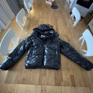 Svart glansig pufferjacka från Nelly - Säljer en svart glansig pufferjacka från Nelly i storlek S. Jackan har en hög krage och dragkedja framtill. Perfekt för kalla dagar när du vill hålla dig varm och snygg. Passar både till vardags och festliga tillfällen. 🖤 org pris mellan 900-1000kr men säljer för 600 (inga märken eller hål eller något)