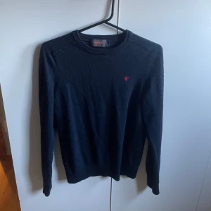 Mörkblå ulltröja från Morris - Säljer en stilren mörkblå tröja från Morris i 100% merinoull. Den har en liten röd broderad logga på bröstet och ribbade kanter vid ärmslut och nederkant. Perfekt för både höst och vinter, och den är i mycket bra skick. Passar både till vardags och lite finare tillfällen. Står S men sitter mera XS