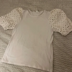 Vit topp med spetsärmar - Säljer en superfin vit topp med puffiga spetsärmar. Perfekt för både vardag och fest! Toppen är i bra skick och har en normal passform. 