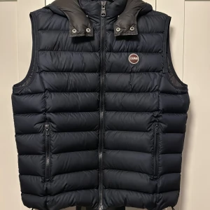 Mörkblå dunväst från Colmar - Säljer en snygg mörkblå dunväst från Colmar i storleken L. Använd 2 gånger men är i absolut nyskick. Västen har en dragkedja framtill och en hög krage för extra värme. Perfekt för höst och vinter, och den quiltade designen ger en stilren look. Passar både till vardags och lite finare tillfällen. Pris går att diskutera :)