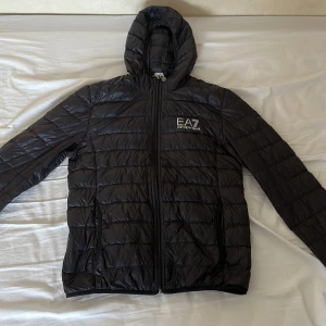 Svart dunjacka från EA7 - Säljer en snygg svart dunjacka från EA7 i mycket bra skick. Jackan har en dragkedja framtill och en praktisk huva. Perfekt för kyliga höst- och vinterdagar. Den är lätt och bekväm att bära, med en stilren design som passar till det mesta. Pris kan också diskuteras vid snabb affär. Hör av dig vid intresse! 