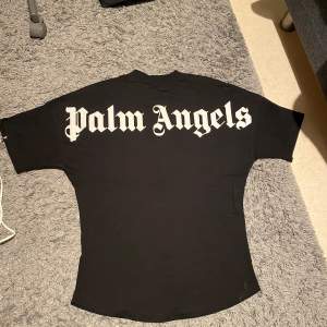 Säljer en svart t-shirt från Palm Angels i mycket bra skick. Den har ett stort, vitt tryck på baksidan och mindre text vid nacken. Perfekt för en casual look eller streetwear-stil. Passar både till vardags och fest!