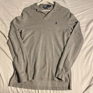 Grå pikétröja från Ralph Lauren - Säljer en stilren grå pikétröja från Ralph Lauren i storlek S. Tröjan har långa ärmar och den klassiska broderade loggan på bröstet. Perfekt för både vardag och lite finare tillfällen. Skön och bekväm passform!