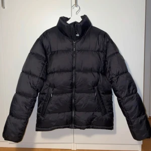 Svart dunjacka från Lindbergh - Säljer en svart dunjacka från Lindbergh i mycket bra skick. Jackan har en dragkedja framtill och långa ärmar. Perfekt för kalla vinterdagar. Den är både stilren och varm, vilket gör den till ett måste i garderoben. Passar lika bra till vardags som till mer uppklädda tillfällen. Tveka inte på att skriva om du har några funderingar