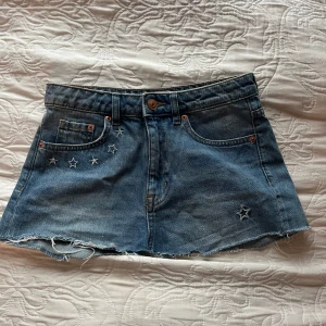 Jeanskjol från H&M Coachella - Superfin jeanskjol från H&M Coachella-kollektionen! Den är blå med coola stjärndetaljer och rå kant nertill. Perfekt för sommarens festivaler eller en dag på stan. Baktill finns broderade stjärnor och texten 'Daydreamer'. Ser ”klippt” ut i kanten