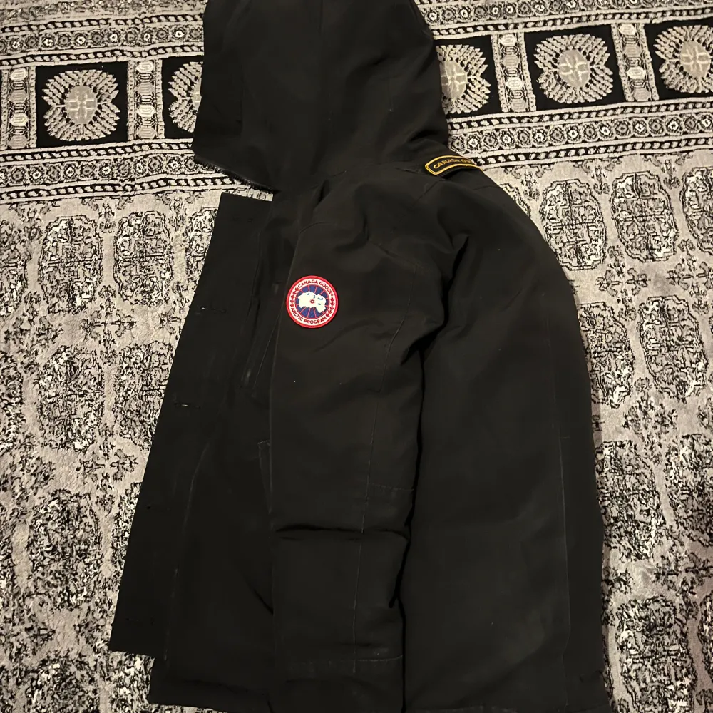 Säljer en svart  från Canada Goose i mycket bra skick. Jackan har en huva och stängs med både dragkedja och knappar. Perfekt för kalla vinterdagar med sin varma och skyddande design. Passar bra för både vardag och utomhusaktiviteter. Pris kan även diskuteras.. Jackor.