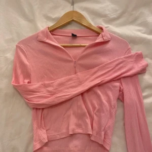 Rosa ribbad tröja med dragkedja - Säljer en superfin rosa ribbad tröja med dragkedja framtill. Den har en croppad stil och långa ärmar, perfekt för både vår och höst. Tröjan är i bra skick och passar perfekt till ett par jeans eller kjol. Perfekt för en casual look! 💖