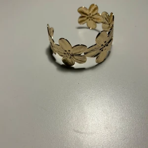 Guldiga smycken i olika stilar - Säljer ett set med guldiga smycken. Första bilden visar ett armband med blommotiv, perfekt för en somrig look. Andra bilden har små, eleganta örhängen med en vriden design. Tredje bilden visar örhängen med blixtmotiv! Fjärde bilden visar tre olika armband, ett med kedja, ett slätt och ett med små detaljer. Alla smycken är i mycket bra skick och passar till både vardag och fest. Allt är rostfritt stål och aldrig använt! Säljer för 40 kr st