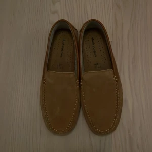 Bruna Hush Puppies loafers i mocka - Säljer ett par snygga bruna loafers i mocka. De har en klassisk design med stilrena sömmar och är perfekta för både vardag och fest. Skorna är i mycket bra skick och passar perfekt till höst- och våroutfits. Storlek herr 42. Köparen står för frakt. Ny pris 1600, pris kan diskuteras.