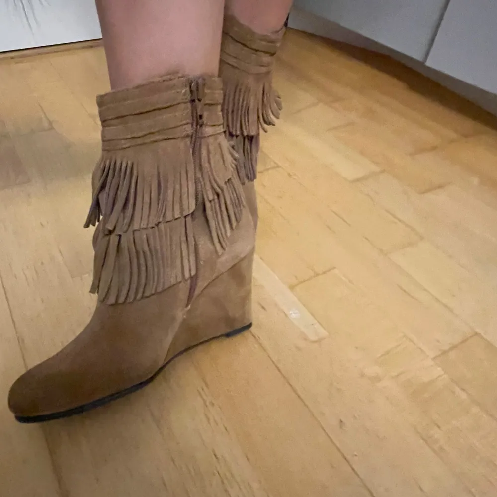 Snygga bruna boots i mocka med fransar och dragkedja på sidan. Perfekta för hösten med en bekväm kilklack som ger lite extra höjd. De har en cool boho-vibe och passar perfekt till både jeans och klänning.. Skor.