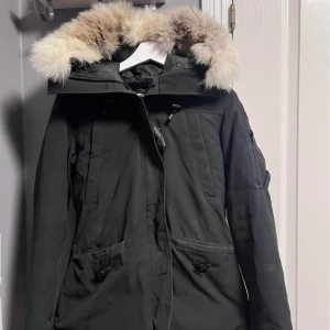 Canada goose montebello - Säljer en svart parkajacka från Canada Goose med en mysig pälsfodrad huva. Jackan har en dragkedja och flera praktiska fickor. Perfekt för kalla vinterdagar. Den är i bra skick och redo för nya äventyr! 🖤
