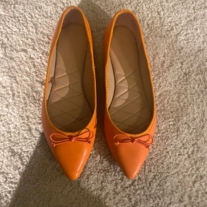 Orange ballerinaskor med rosett - Säljer ett par snygga orange ballerinaskor i mycket bra skick. De har en spetsig tå och en söt rosett framtill. Perfekta för vår och sommar! Skorna är bekväma och stilrena passar både till fest men också vardaglig användning❤️💕