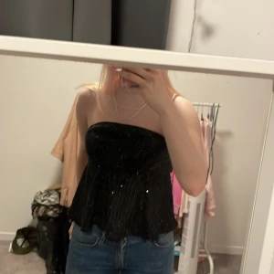 Svart glittrig tubtopp - Säljer en snygg svart tubtopp med glittriga detaljer. Perfekt för festliga tillfällen! Toppen är axelbandslös och har en luftig passform som ger en fin siluett. Passar perfekt till jeans eller kjol för en chic look. 🖤✨